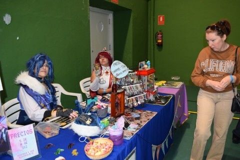 Una visitando mirando el puesto de dos artistas disfrazadas del juego de 'Genshin Impact'