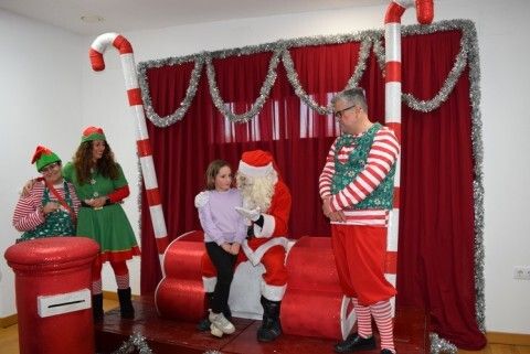 Papá Noel hablando una niña en sus rodillas acompañado de sus elfos