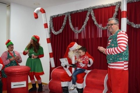 Papá Noel hablando un niño en sus rodillas acompañado de sus elfos