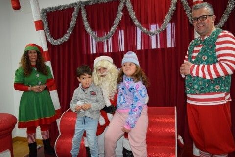 Papá Noel tomándose una foto un niño en sus rodillas acompañado de sus elfos